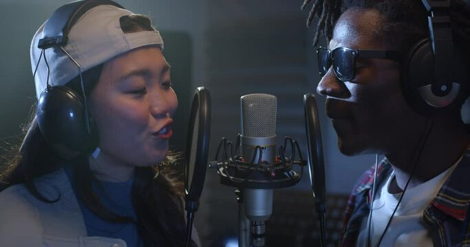 Close Up on Two Multiethnic Professional Singers Recording a New Album in a Studio. Talented Black Male and Asian Female Young Artists Collaborating and Singing Together a Romantic Song