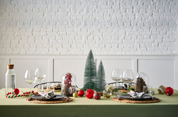 Christmas and new year dinner table serving, green tablecloth, accessory, tree, interior, white brick wall.