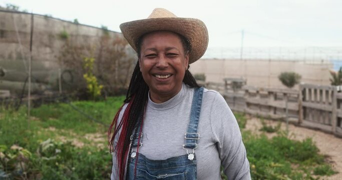 African senior woman smiling on camera outdoor at organic vegetables plantation - Local food product and sustainable work concept