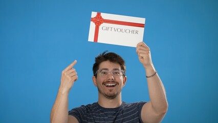Portrait of smiling happy handsome young man striped t-shirt holding gift certificate voucher coupon isolated on blue background in studio.