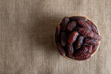 Date fruits in wooden bowl on burlap sack,top view
