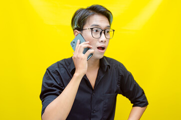 overjoyed young asian man with peek a boo colored hair wearing black shirt holding phone. Young Asian man with a pleasing smile using a smartphone for trading or chatting.