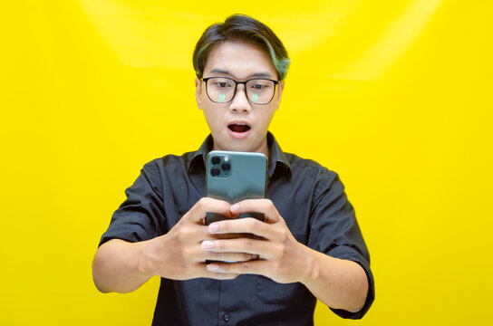 overjoyed young asian man with peek a boo colored hair wearing black shirt holding phone. Young Asian man with a pleasing smile using a smartphone for trading or chatting.