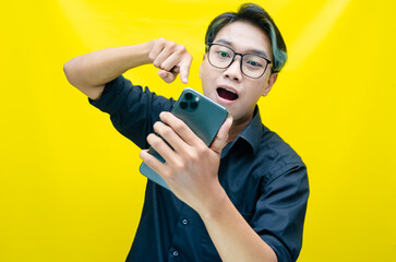 overjoyed young asian man with peek a boo colored hair wearing black shirt holding phone. Young Asian man with a pleasing smile using a smartphone for trading or chatting.