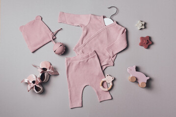 Pastel bodysuit, pants, hat, bib, shoes, toys on grey backgroundd. Set of pink baby stuff and accessories for girl. Baby shower concept. Fashion newborn. Flat lay, top view. Copy space