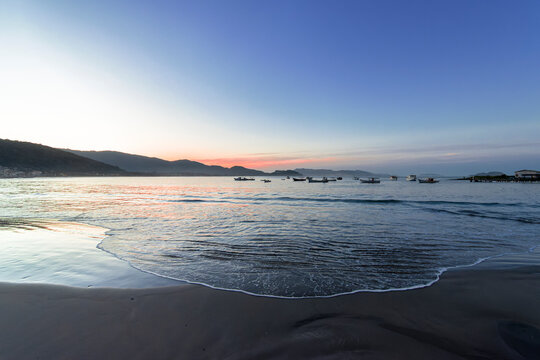 O adeus dourado do sol no horizonte azul. Um fim de tarde na praia com ondas calmas e um c&eacute;u azul e laranja