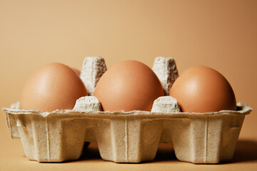 A tray with brown eggs, on a nude background, chicken feathers are flying. Eco products, nutrition, proteins and natural food.