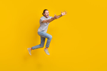 Fototapeta na wymiar Full length photo of positive excited guy dressed grey t-shirt jumping high holding arms empty space isolated yellow color background