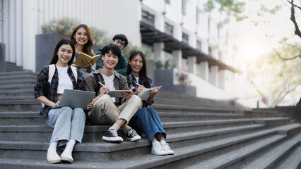 Group of cheerful Asian college students sitting on stairs, showing fists, celebrating triumph