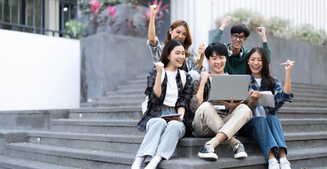 Obraz premium Group of cheerful Asian college students sitting on stairs, showing fists, celebrating triumph