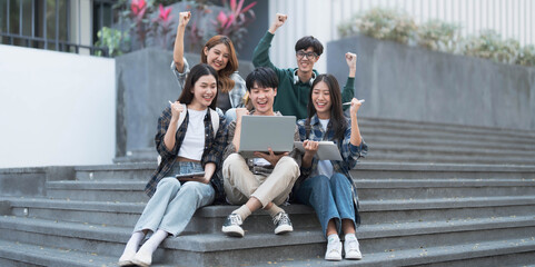 Obraz premium Group of cheerful Asian college students sitting on stairs, showing fists, celebrating triumph