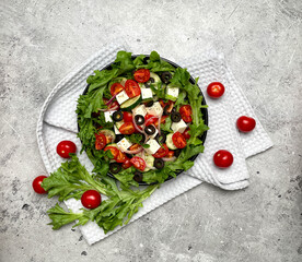 Greek salad with tomatoes, cucumbers, olives, feta cheese, herbs in a plate. Top view.