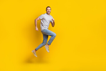 Fototapeta na wymiar Full length photo of excited funky guy dressed grey t-shirt jumping high running fast empty space isolated yellow color background