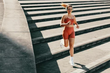 Tuinposter Athletic female using music to enhance running and jogging outdoor stairs workout © Jacob Lund