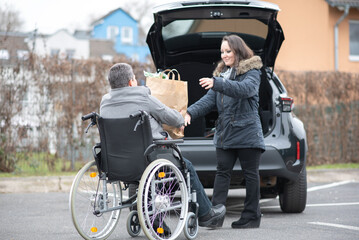A woman helps a disabled person on a wheelchair to pack groceries into the car