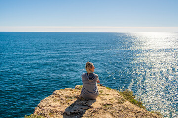 Naklejka na ściany i meble A woman enjoying the ocean view from the top of cliffs at Marinha Beach in Algarve, Portugal