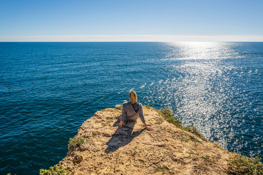 A woman enjoying the ocean view from the top of cliffs at Marinha Beach in Algarve, Portugal