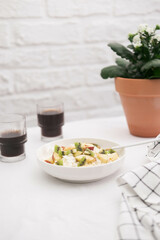 Cottage cheese with fruits and honey in a white plate with a spoon and a napkin, two glasses of coffee and pot with flowers on a white background. Healthy breakfast.