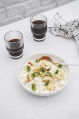 Cottage cheese with fruits and honey in a white plate with a spoon and a napkin, two glasses of coffee on a white background. Healthy breakfast.