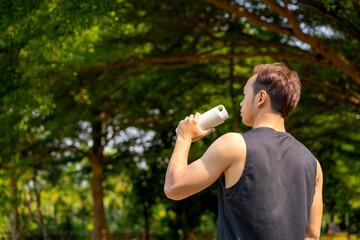sporty handsome man drinking water after jogging in city public park during summer day, young guy...