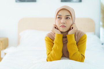 Unhappy - stressful Asian young muslim woman sitting alone on the bed in the morning. Asian muslim woman having a mental burn out or depression problem from working and social environment.