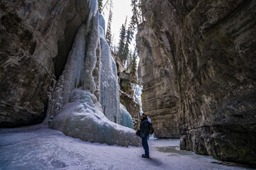 man tourist with beard in sunglasses looking on blue ice of frozen waterfall in maligne river stone canyon 