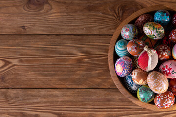 Obraz na płótnie Canvas A wooden bowl with closely arranged Easter eggs stands on a background of boards.