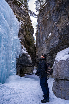 man tourist with beard in sunglasses looking on blue ice of frozen waterfall in maligne river stone canyon 