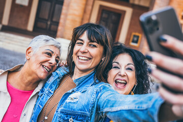 Happy females senior friends taking selfie shot with smart phone outdoors on urban city street- Group of three aged women enjoying together on holiday - Lifestyle Tourist Concept with mature people