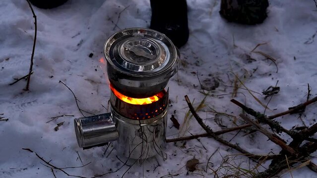 Fire burns in march mini stove on snow in winter forest camp