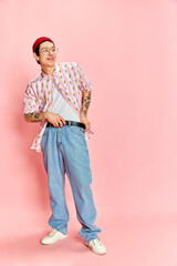 Fototapeta premium Full length photo of stylish guy with tattoo fastening his belt and looking away over pink background. Concept of fashion, youth, student life