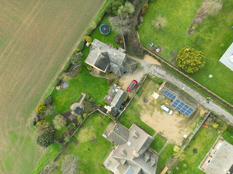 Drone Top Down View Of A Large Detached House Showing Solar Panels On Its Detached Garage. Located In The English Countryside At The Edge Of An Expanding Village.