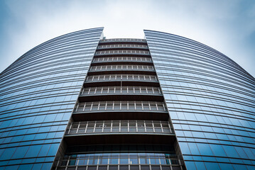 Curvilinear facade of a modern skyscraper in the financial district of Milan, Italy. Blue lattice facade with glass windows, with a cloudy background.