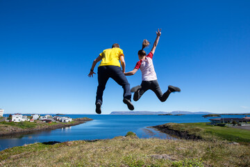 Happy people, enjoy your life! Two people in love are jumping into the air in beautiful nature of Stykkiholsmur, Iceland in sunny weather near a sea, ocean, travel the world