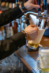 Fototapeta na wymiar man bartender hand at beer tap pouring a draught beer in glass serving in a restaurant or pub