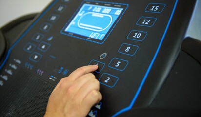 Closeup shot of a female pushing a bottom on a treadmill gym equipment