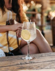 Refreshing lemonade in a wine glass on a wooden table in front of a woman in the beach bar.