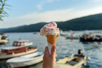 Fototapeta premium Selective focus shot of a hand holding an ice cream in a cone with moored boats in the sea