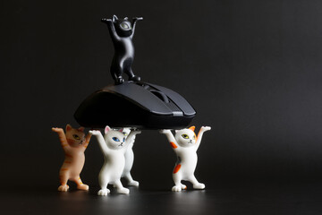 Five cute toy kittens with raised paws and a gray computer mouse on a dark background. A humorous concept about cats hunting mice. Toy world. copy space. Selective focus