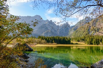 Scenic landscape of Lake Fusine with shallow water surrounded by lush trees against steep mountains