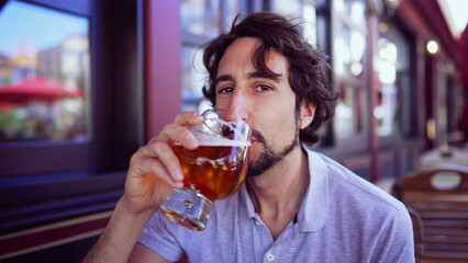 Happy person drinking beer outdoors smiling at camera. Portrait of one young man holding glass of alcohol drink