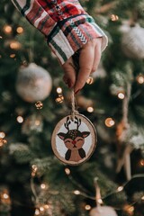 Female hand holding diy wooden handpainted christmas ornament in front of christmas tree
