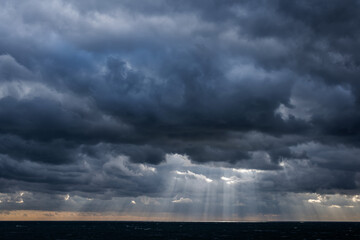 Distant sun rays through dark storm clouds over a dark sea