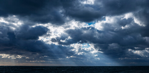 Fototapeta na wymiar Panoramic view of the sunrays through the stormy clouds over the dark sea