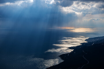 Sun rays through dark clouds over the shining sea and dark coast, top view