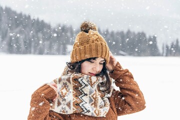 Woman in a cozy winter sweater and scarf looking down under falling snow in the wilderness