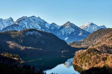 Naklejka na ściany i meble Breathtaking view of Lake Alpsee in Schwangau, Germany with snowy mountains looming over the water