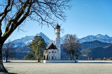 St. Coloman church in Schwangau, Germany surrounded by forests and snowy mountains on a sunny day