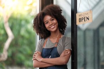 Successful african woman in apron standing coffee shop door. Happy small business owner holding...