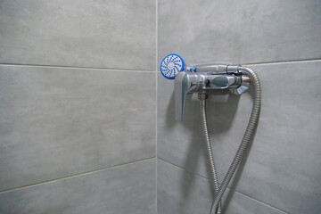 Shower head in bathroom, chrome faucet and grey tiles on walls